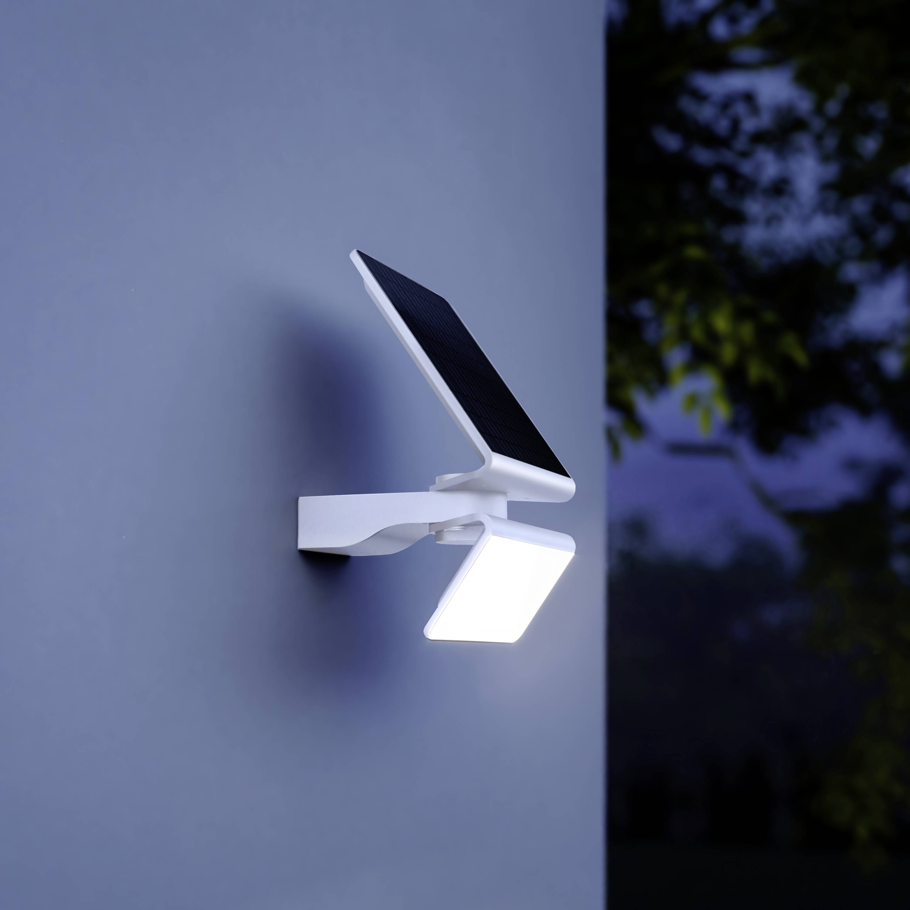 Une lampe murale moderne avec module solaire s'illumine dans l'obscurité. La lampe est fixée sur un mur extérieur gris.