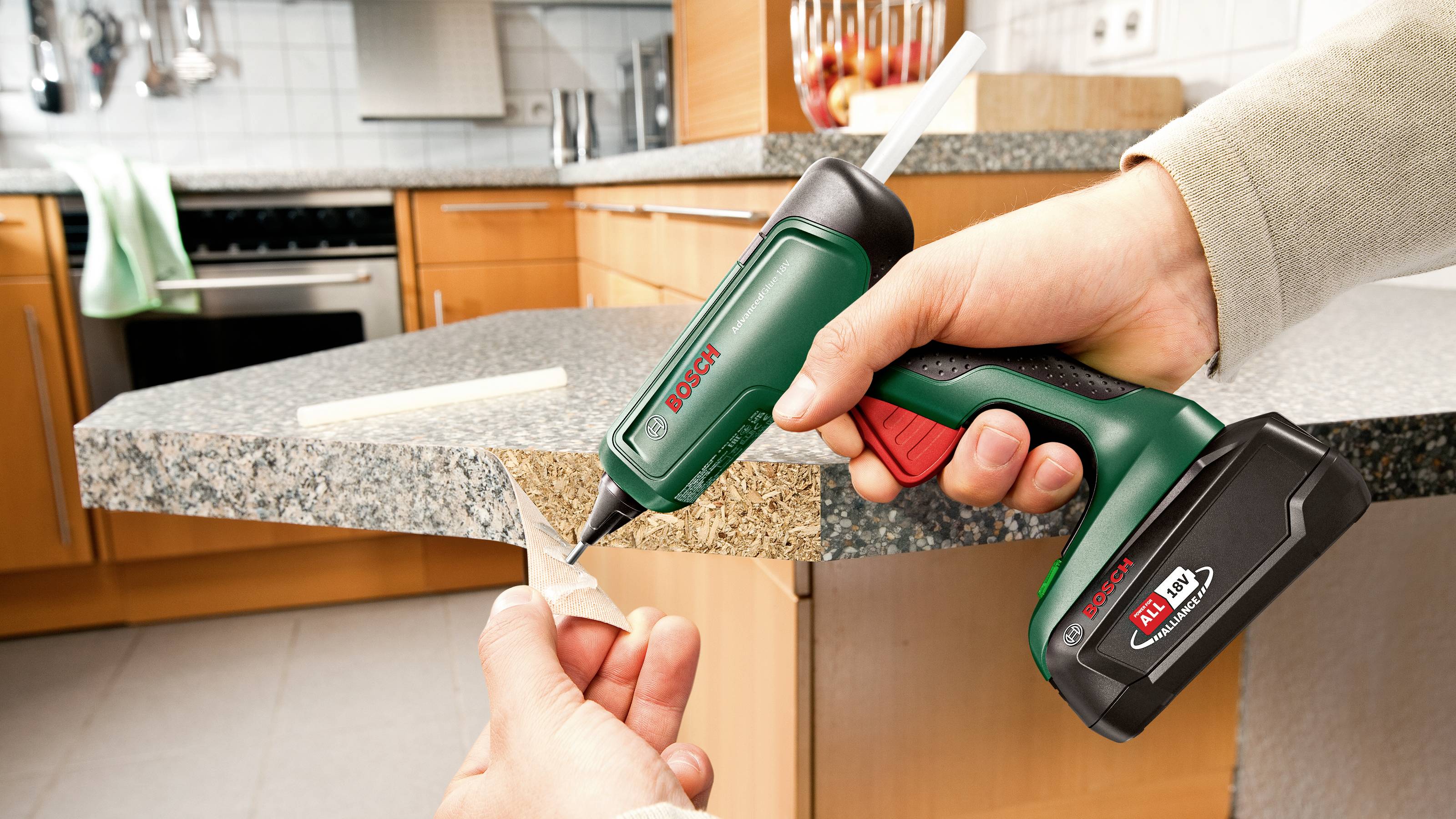 Une personne utilise un pistolet à colle chaude sans fil pour fixer un morceau de bois sur le bord d'un plan de travail de cuisine.