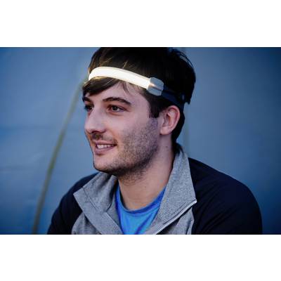 Un homme souriant porte un bandeau frontal avec une LED luminescente. L'arrière-plan est flou et bleu.