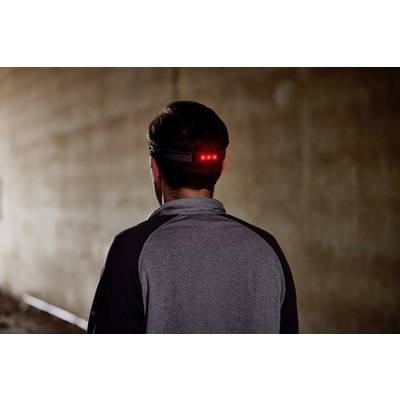 Une personne portant un haut gris marche dans un tunnel sombre. Une lumière rouge brille à l'arrière de son bandeau frontal.