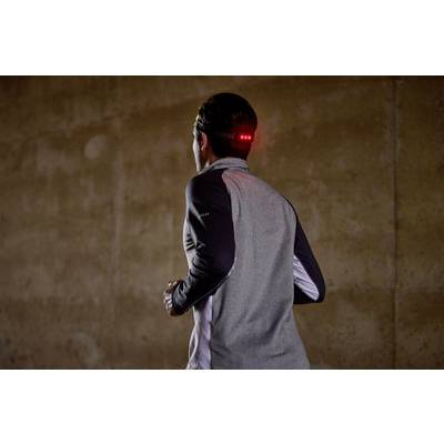 Une personne fait du jogging dans une pièce sombre, portant un haut gris avec des éléments réfléchissants et une lampe LED lumineuse sur la tête.