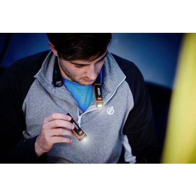 Un homme tient une petite lampe de poche qui éclaire alors qu'il est assis dans une tente. Il porte un pull gris.