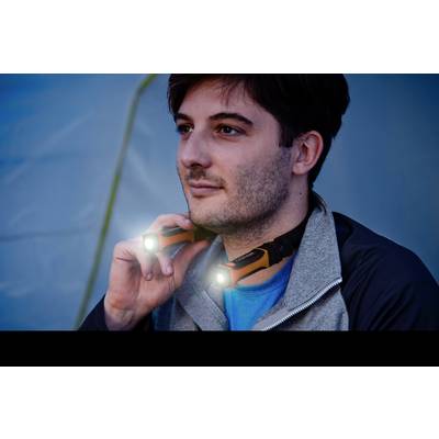 Un homme porte une lampe frontale à l'extérieur. La lampe émet deux lumières vives alors qu'il observe attentivement au loin.