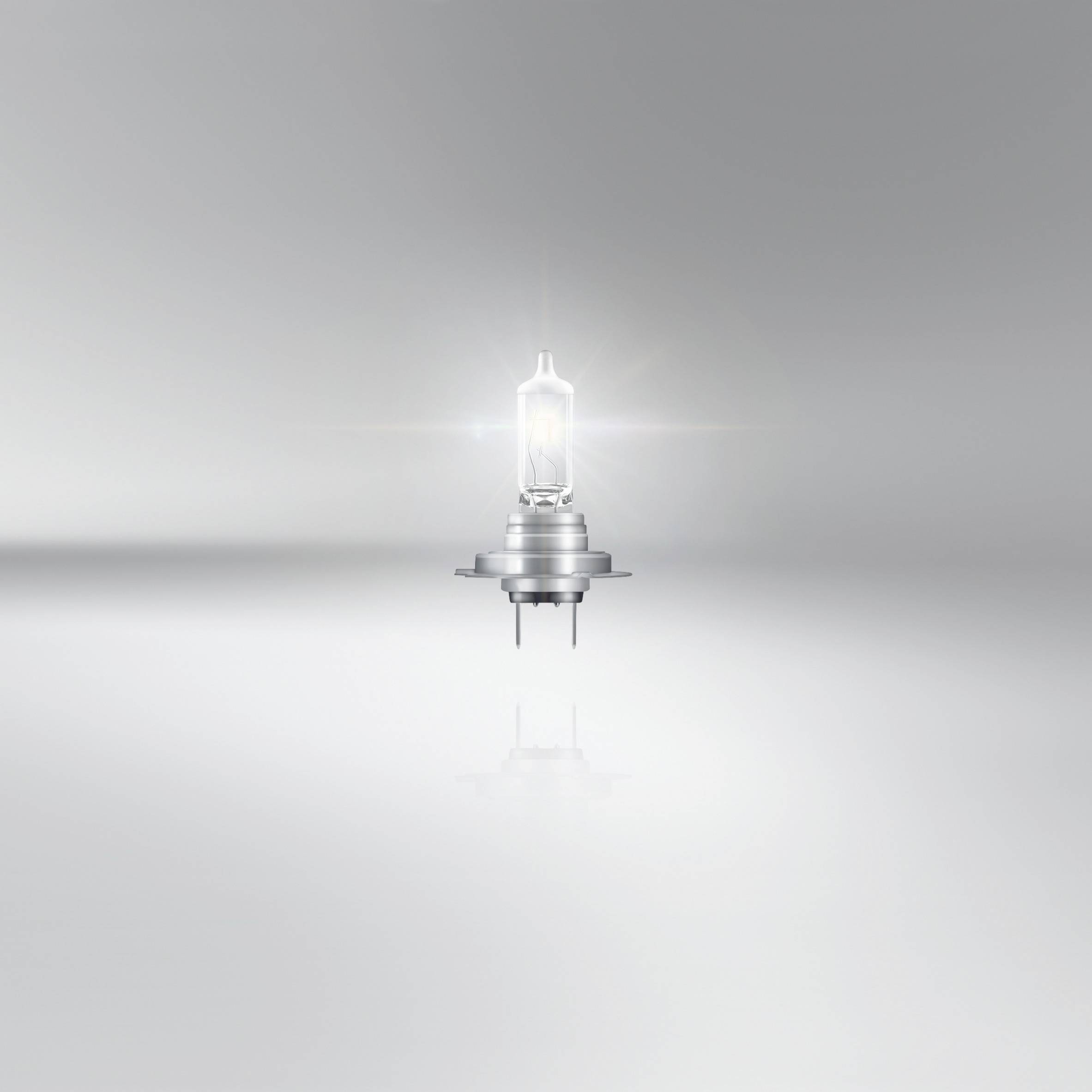 Ampoule sur un fond gris, placée au centre de l'image, légèrement illuminée et se reflétant sur la surface en dessous.