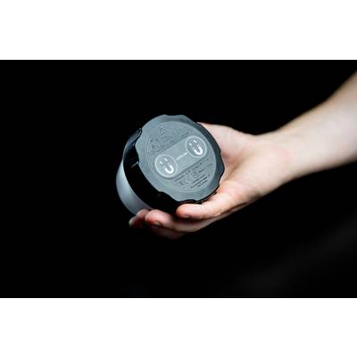 Une main tient un objet rond noir avec deux prises et des symboles sur le dessus. L'arrière-plan est noir.