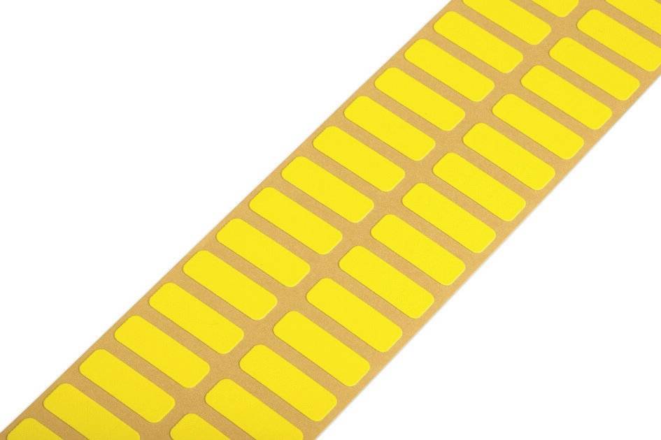 Étiquettes rectangulaires jaunes disposées en rangées régulières sur un rouleau, placées sur du papier support brun, prêtes à être utilisées.