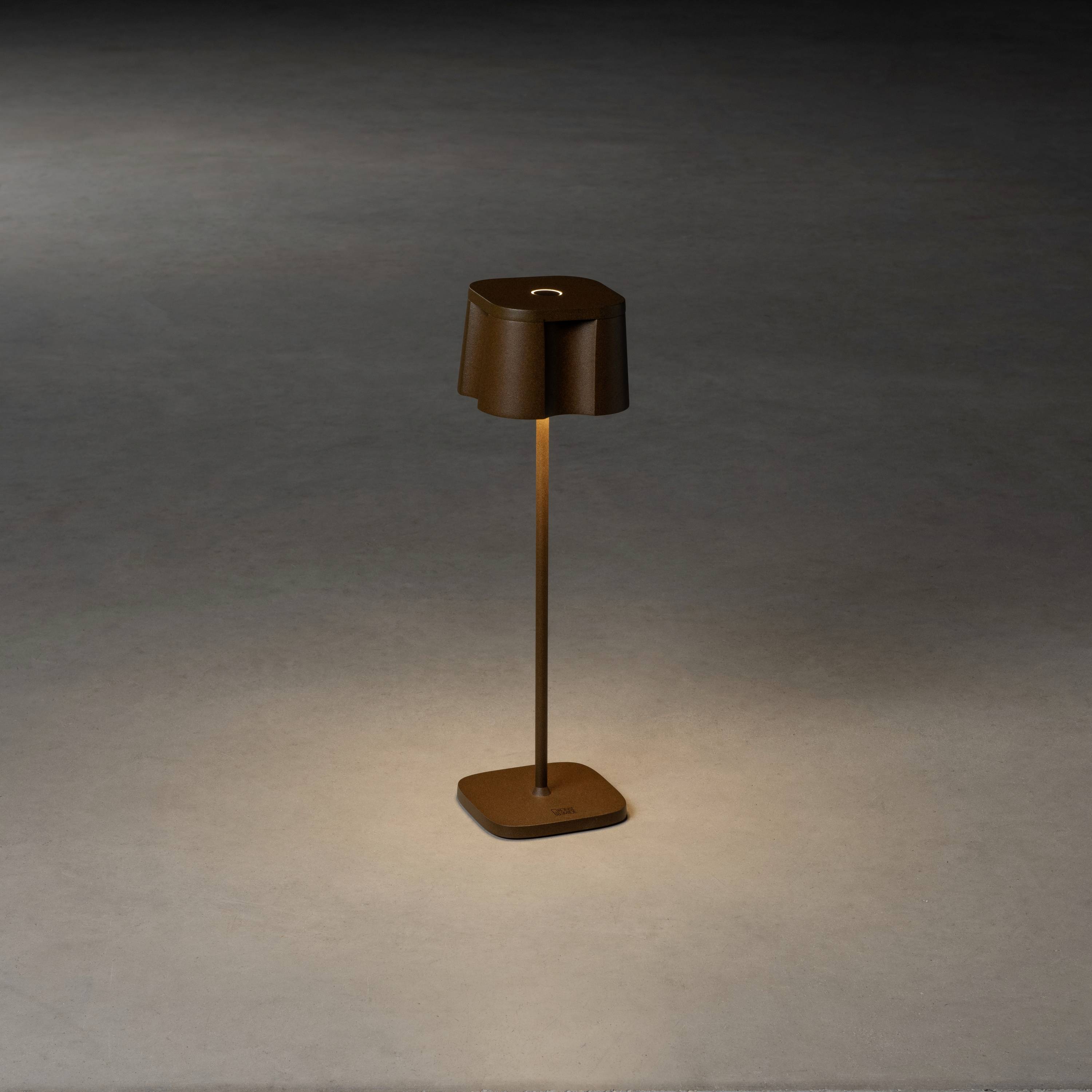 Une lampe moderne et élégante en métal avec un abat-jour brun se trouve dans une pièce faiblement éclairée et diffuse une lumière chaleureuse.