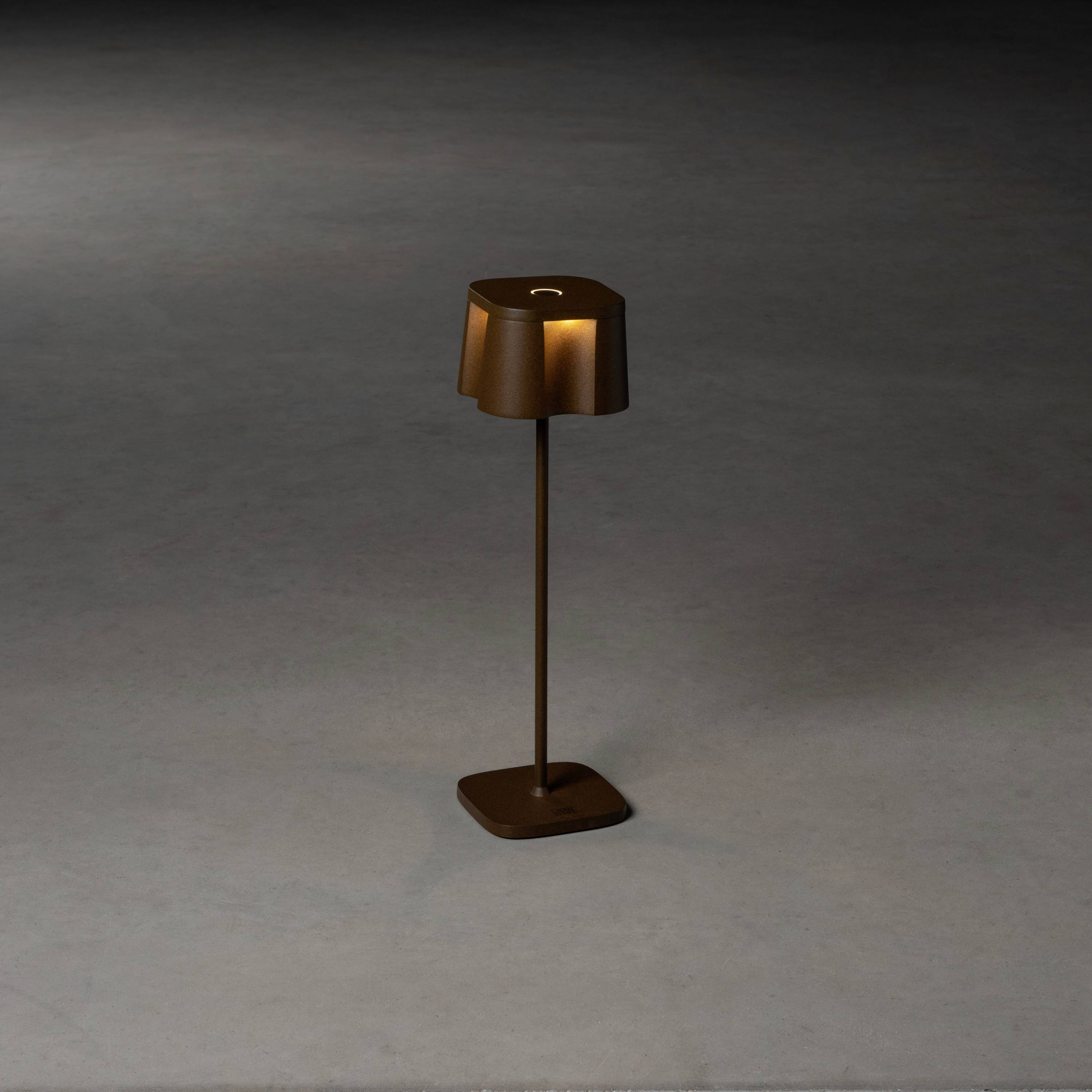 Une lampe sur pied minimaliste de couleur brune se trouve sur un sol gris. Elle est dotée d'un abat-jour plat qui diffuse la lumière vers le bas.