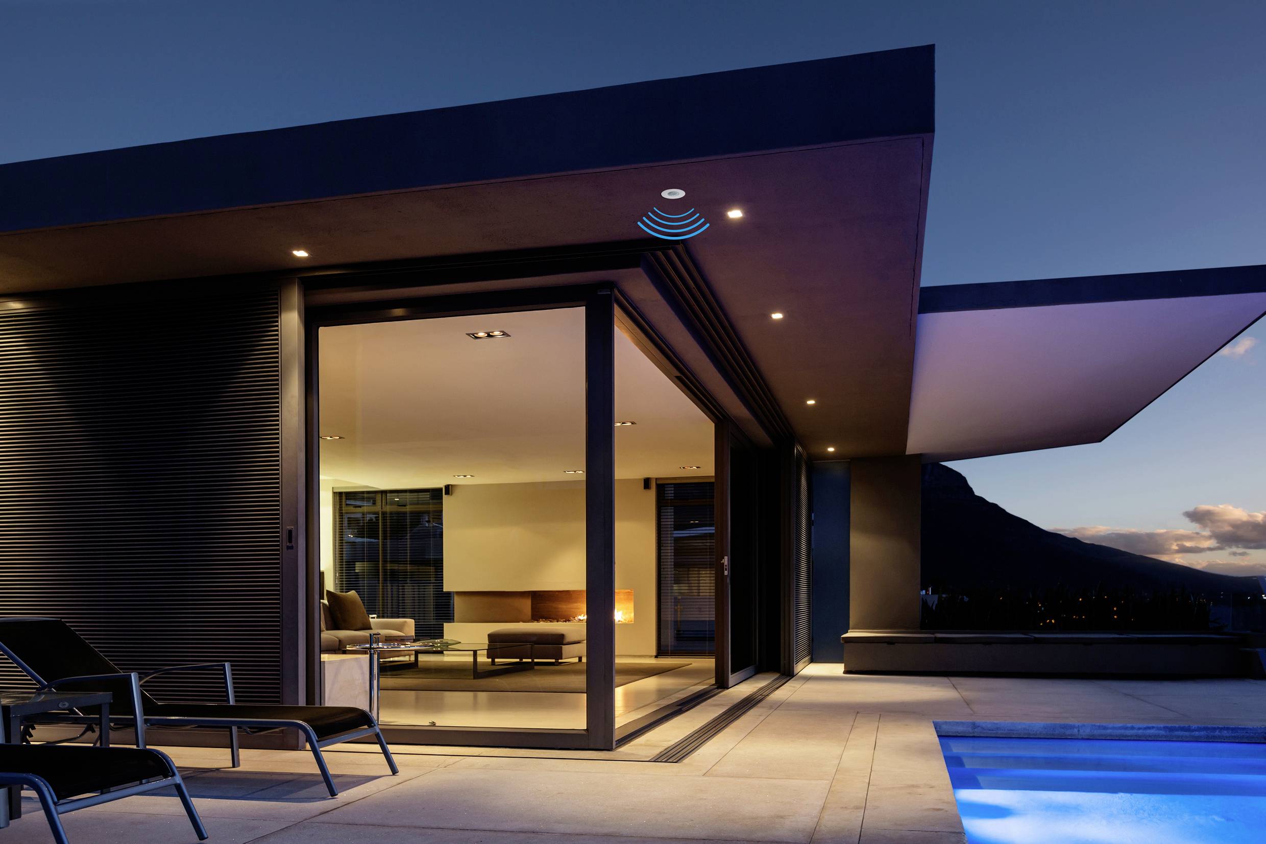 Maison moderne avec des murs de verre et une piscine au premier plan au coucher du soleil, architecture épurée avec une terrasse ouverte.