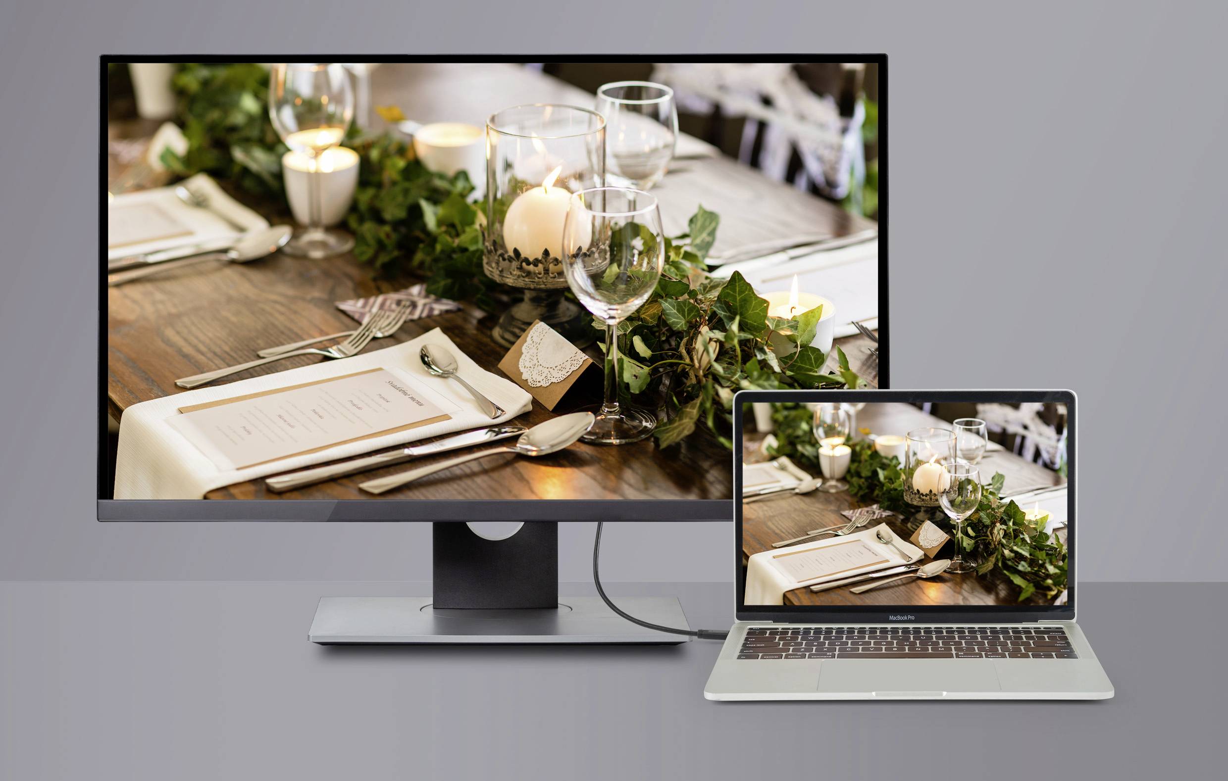 Une table dressée avec des couverts, une carte de menu et des bougies dans des verres, représentée sur un écran de moniteur et un ordinateur portable.