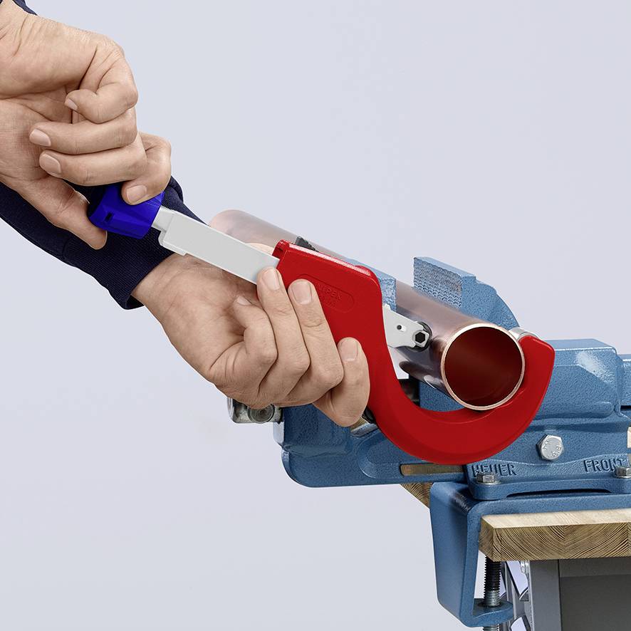 Quelqu'un utilise un outil de coupe de tuyaux rouge pour couper un tuyau métallique dans un étau bleu.