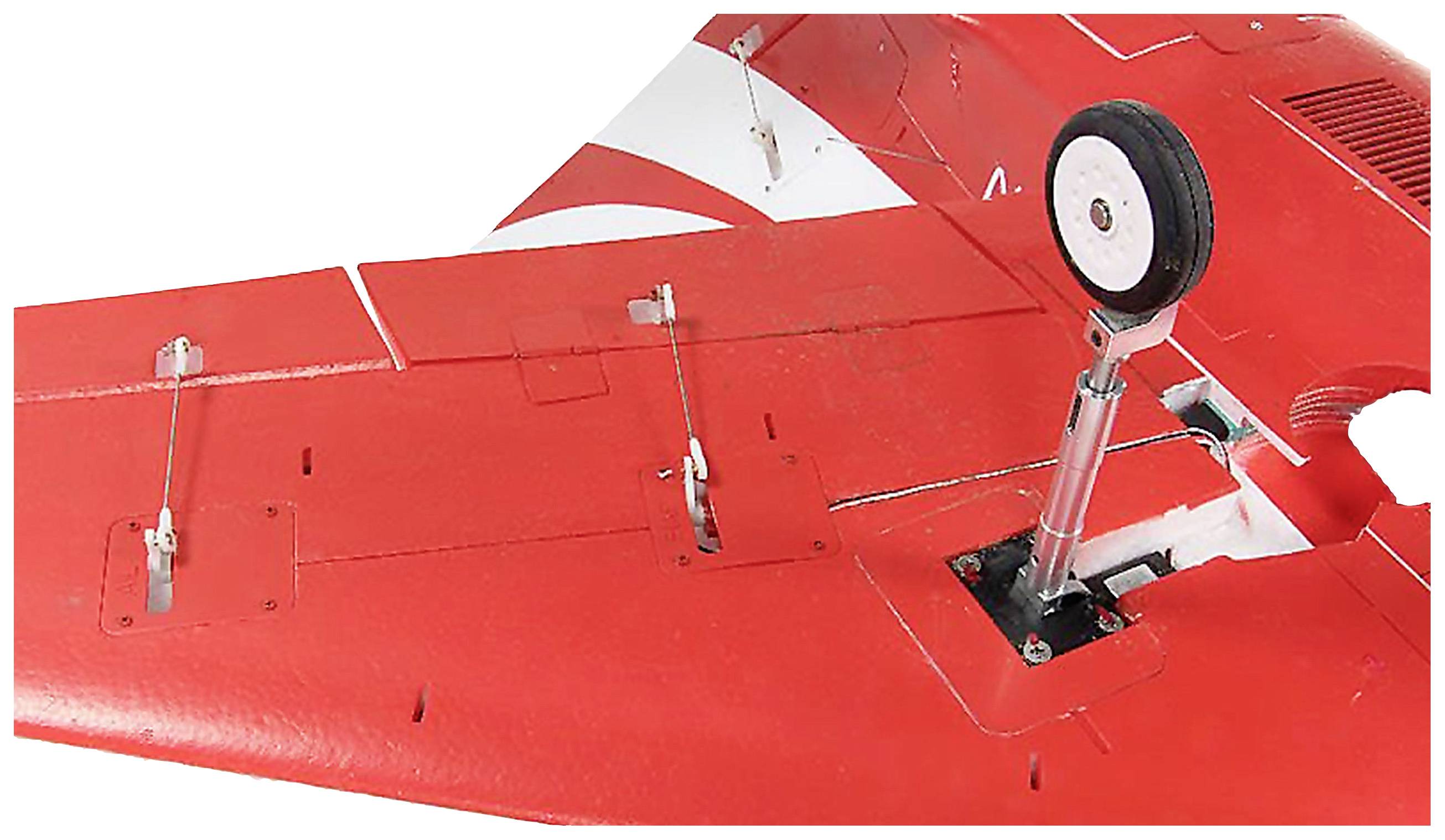 Gros plan sur une aile d'avion rouge avec le train d'atterrissage sorti. L'aile présente des marquages blancs et une construction détaillée.