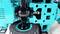 Un robot ou engin de construction de couleur turquoise avec un engrenage visible et une articulation noire. L'accent est mis sur la mécanique technique.