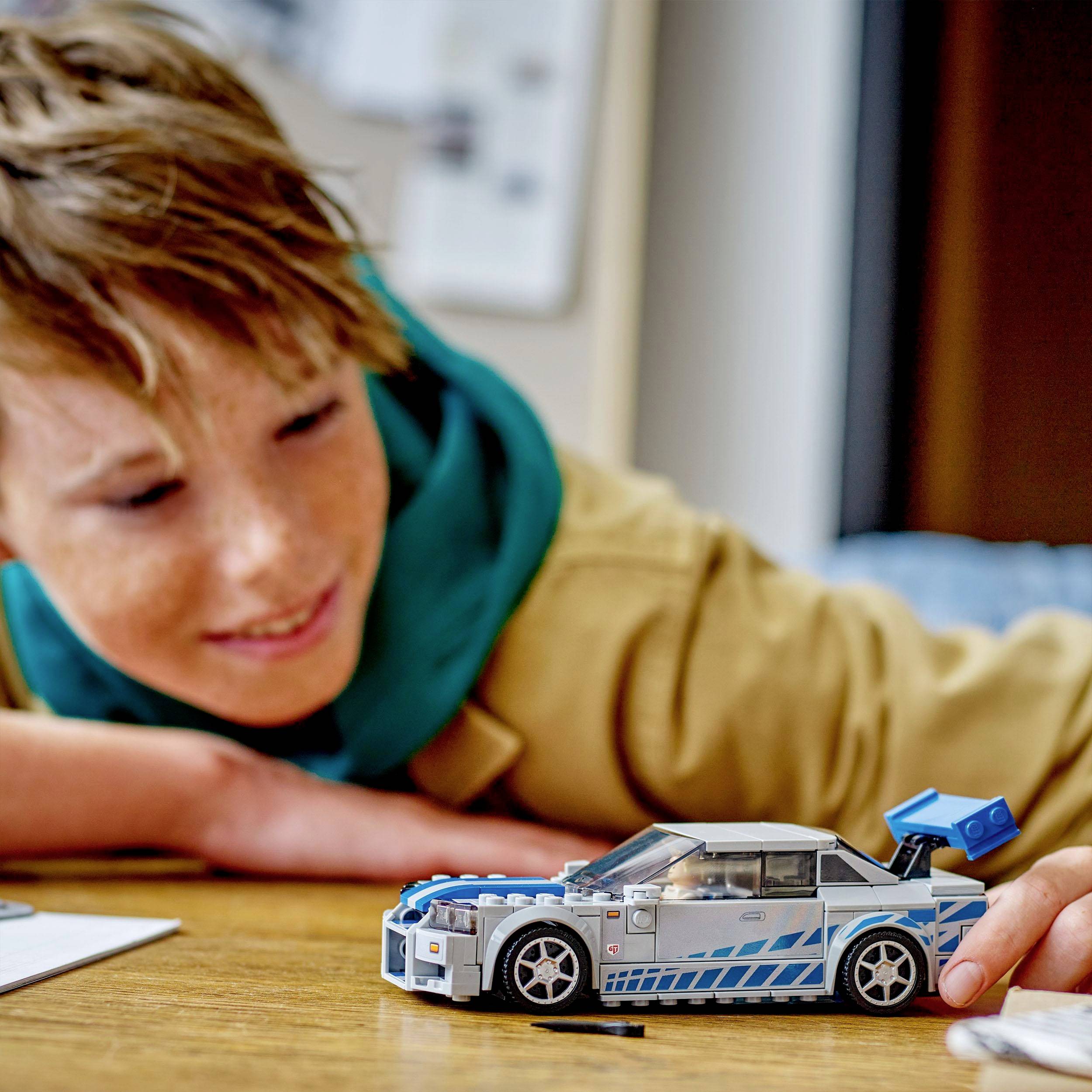 Un enfant regarde avec enthousiasme une petite voiture miniature construite en blocs, posée sur une table en bois.