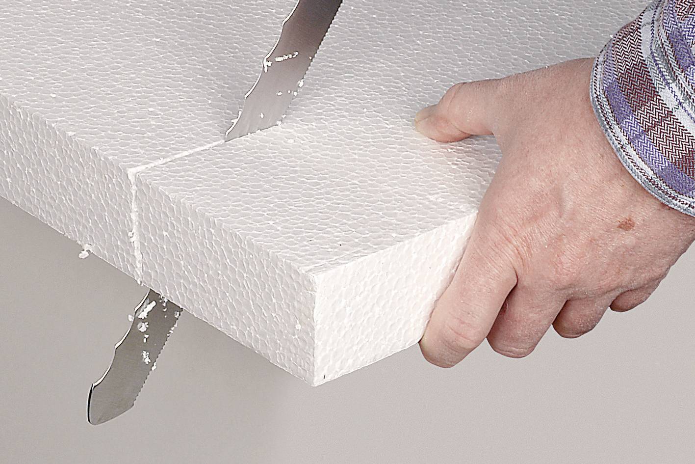 Une main tient une plaque de polystyrène blanche pendant qu'elle est coupée avec un couteau dentelé.