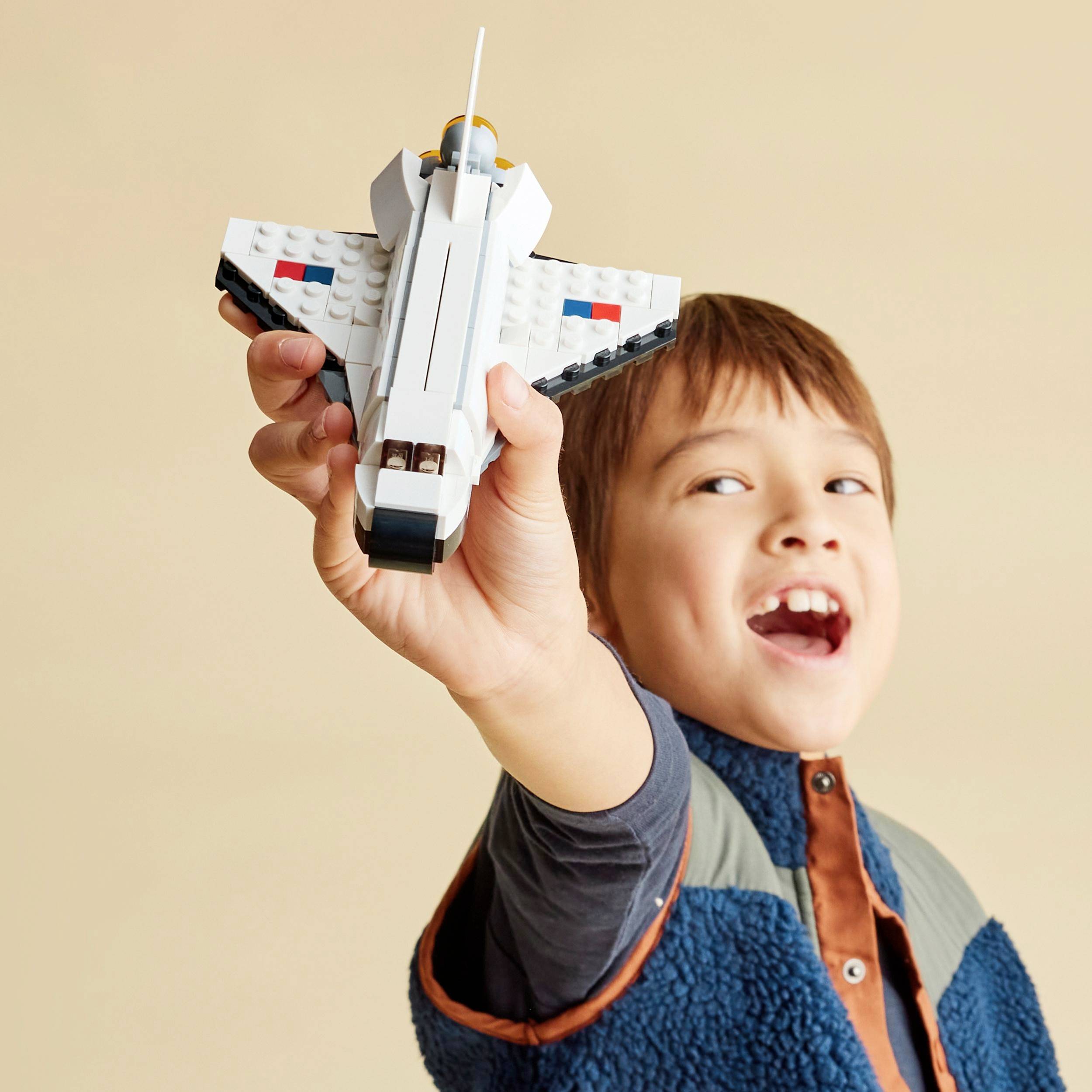 Un enfant tient avec enthousiasme un vaisseau spatial jouet construit avec des blocs de construction colorés et regarde en riant vers la caméra.
