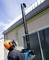 Une personne se tient sur le sol et utilise une machine pour enlever des feuilles d'un toit élevé. La personne porte un casque de protection.