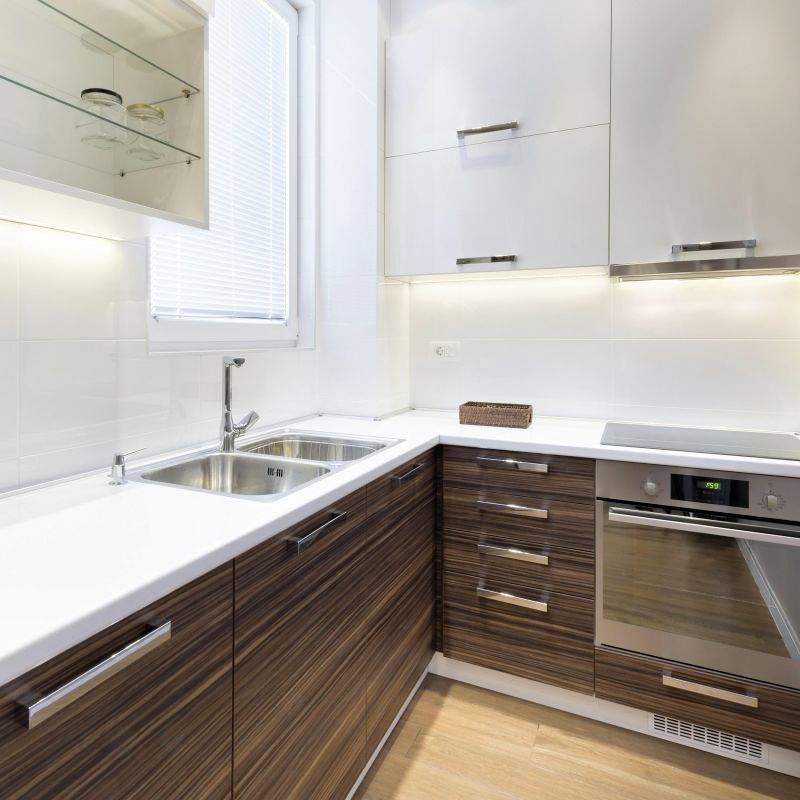 Cuisine moderne avec façades en bois, four encastré, évier et meubles suspendus ; bien éclairée par la lumière naturelle d'une fenêtre.