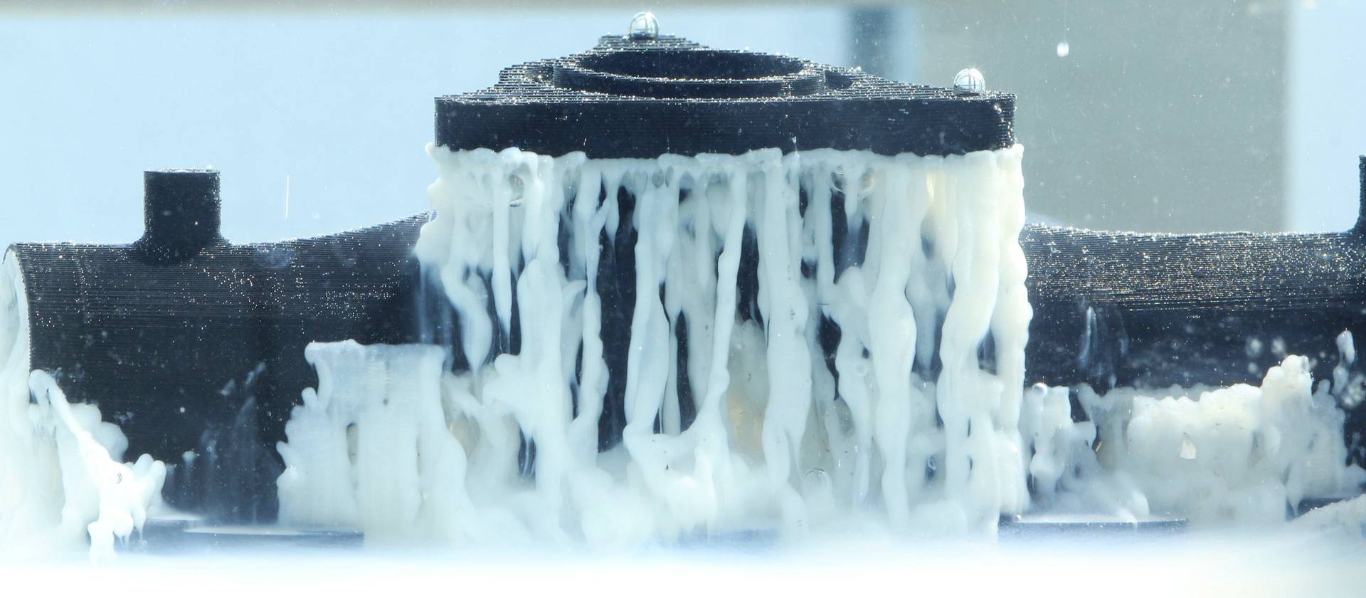 Un objet dans un appareil de test est recouvert d'un liquide, probablement pour des tests de matériau ou d'étanchéité.