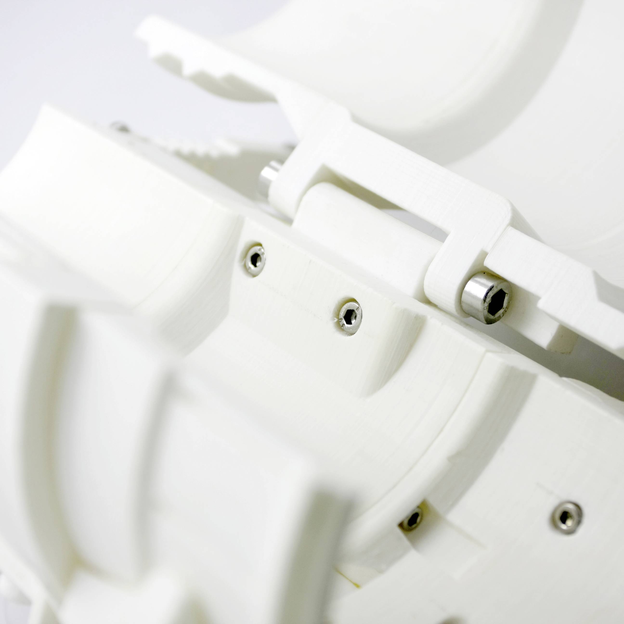 Gros plan d'une structure blanche en plastique avec plusieurs vis et articulations, probablement un composant d'un dispositif technique ou d'une machine.
