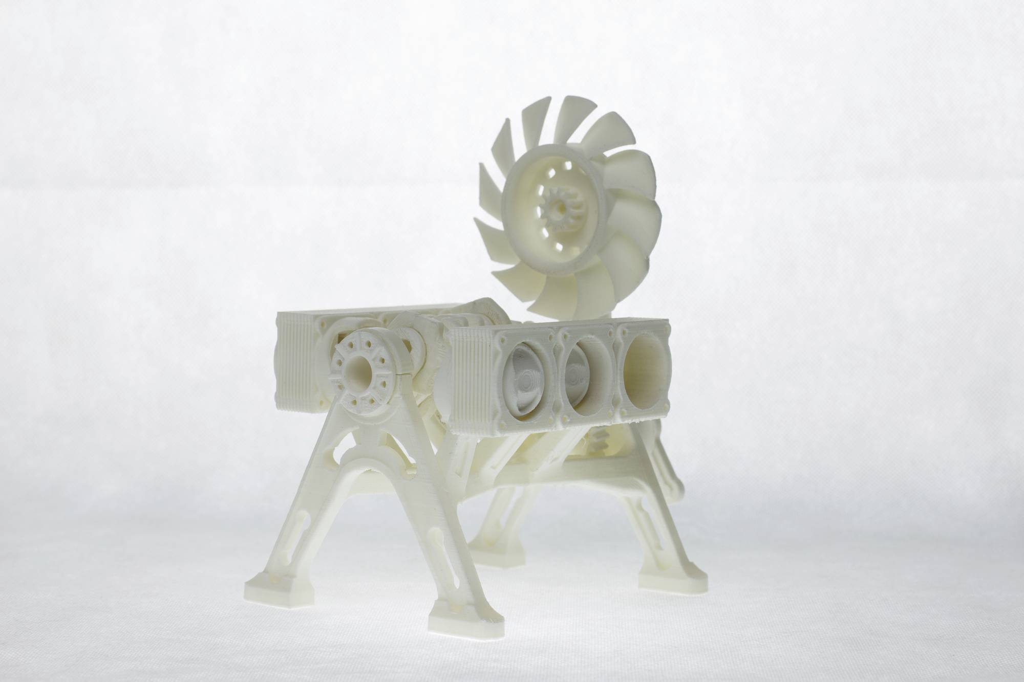 Un modèle complexe imprimé en 3D d'un composant mécanique avec plusieurs pales de ventilateur et des composants cylindriques reposant sur quatre pieds.