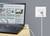 Un ordinateur portable est connecté à une prise réseau par un câble Ethernet, posé sur une table. L'écran affiche des messages et des diagrammes.
