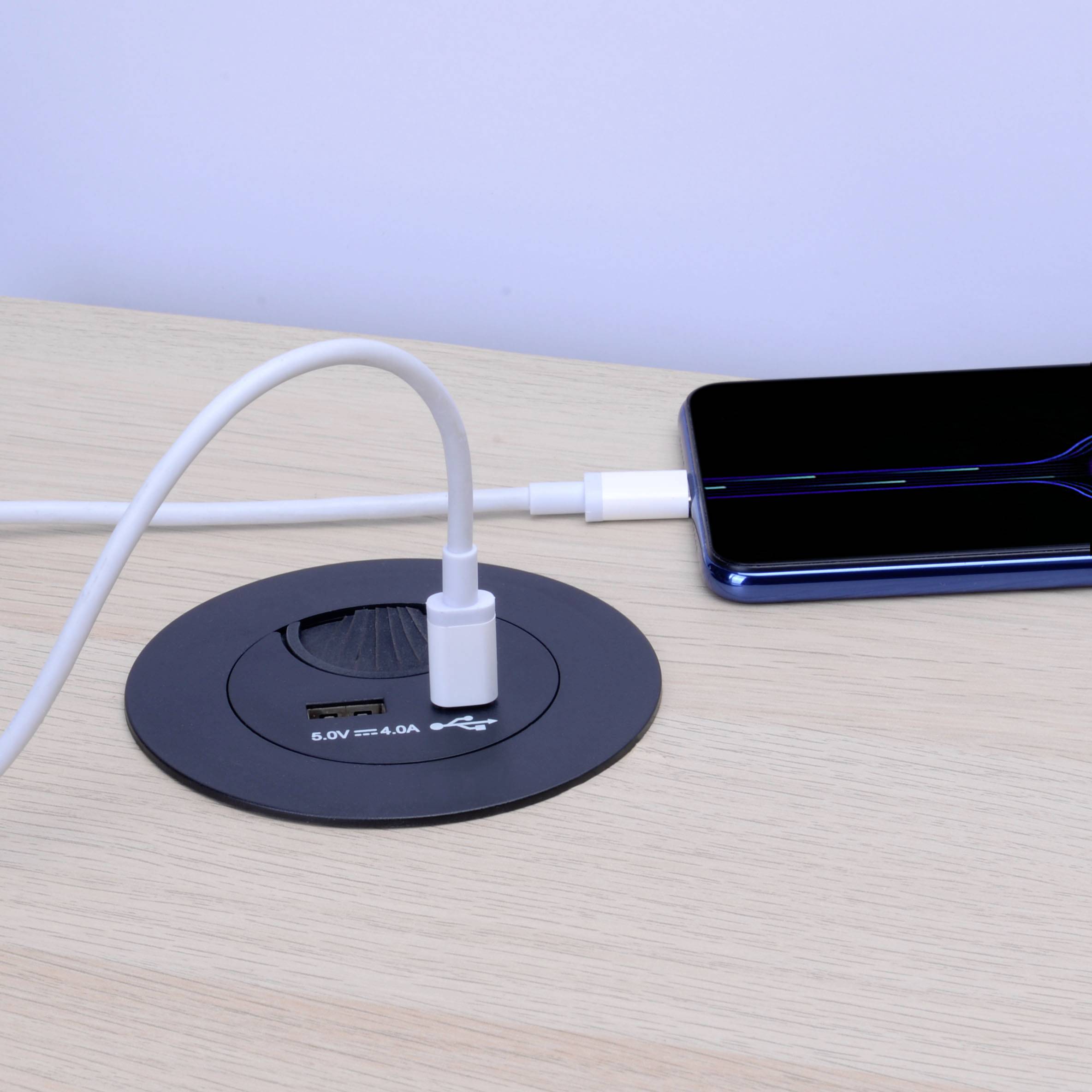 Un smartphone est rechargé sans fil sur une table à l'aide d'un câble de charge intégré et d'un chargeur Qi.