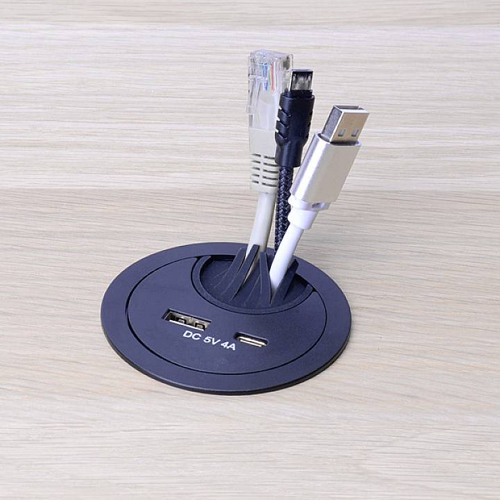 Un passe-câbles dans une table à travers lequel passent quatre câbles : deux câbles USB, un câble Ethernet et un câble à courant continu.