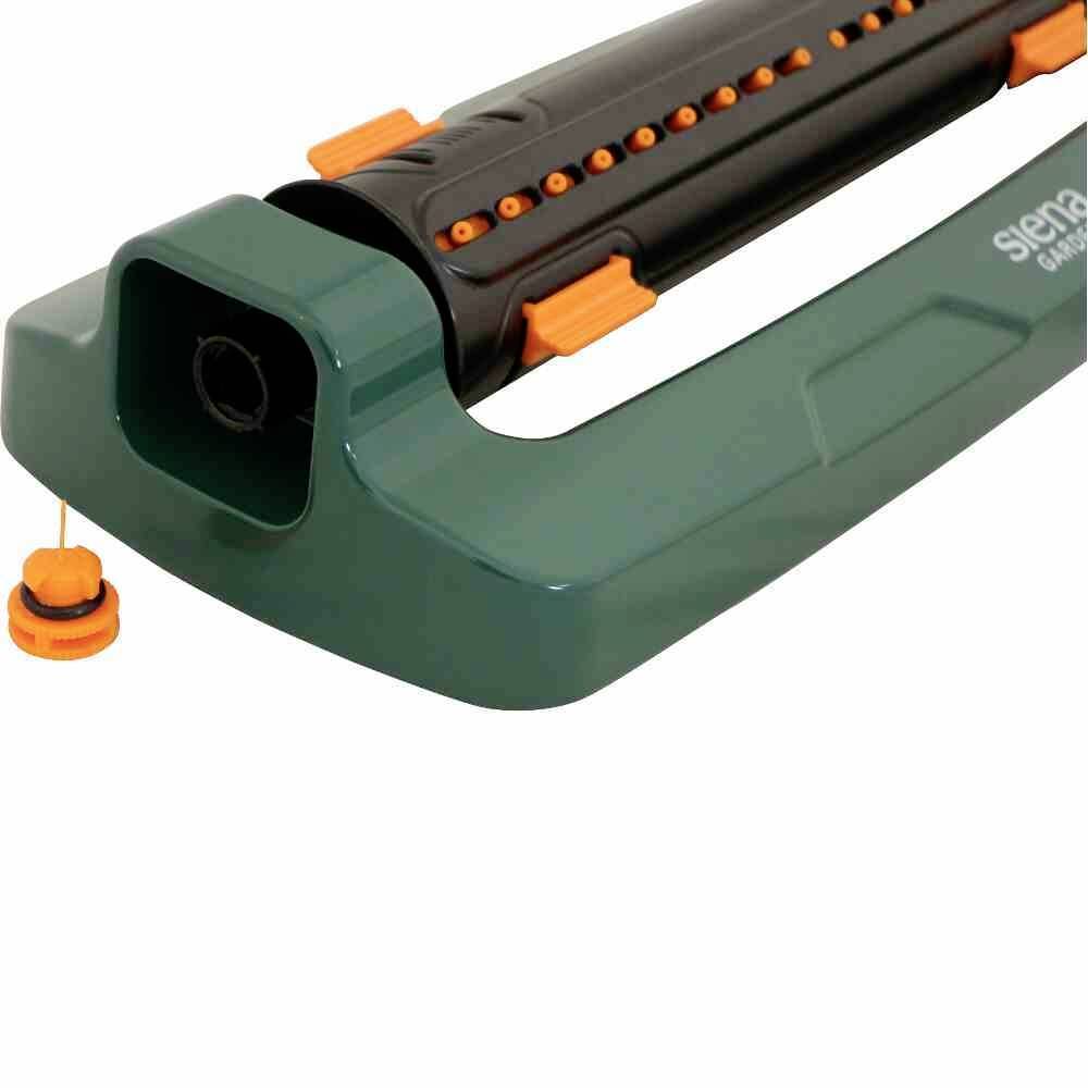 Un arroseur de pelouse vert avec des détails noirs et oranges est posé sur une surface plane. Adapté pour une irrigation uniforme.