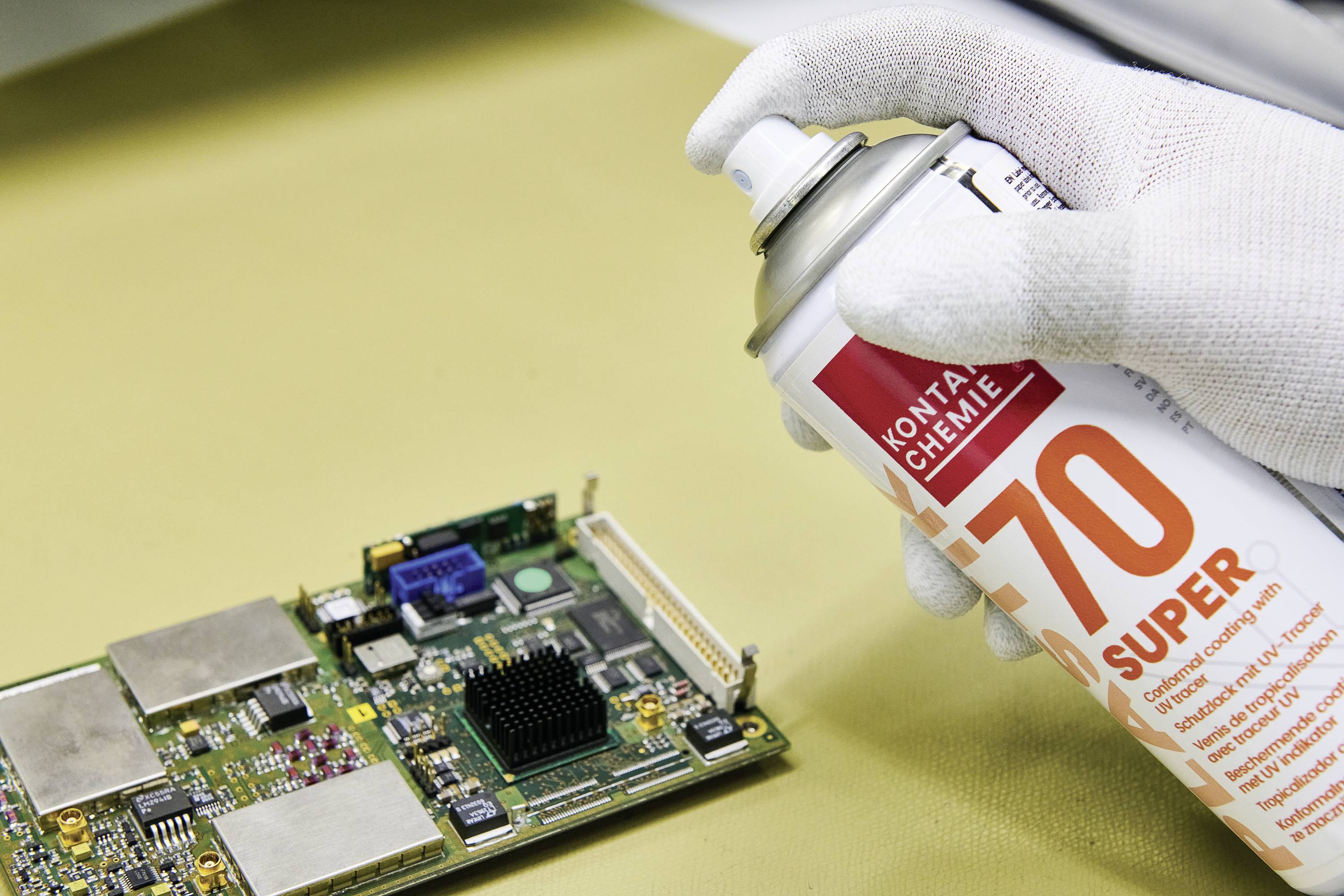 Une main vaporisant un nettoyant en aérosol sur une carte électronique, illustrant un processus de nettoyage pour des composants électroniques.