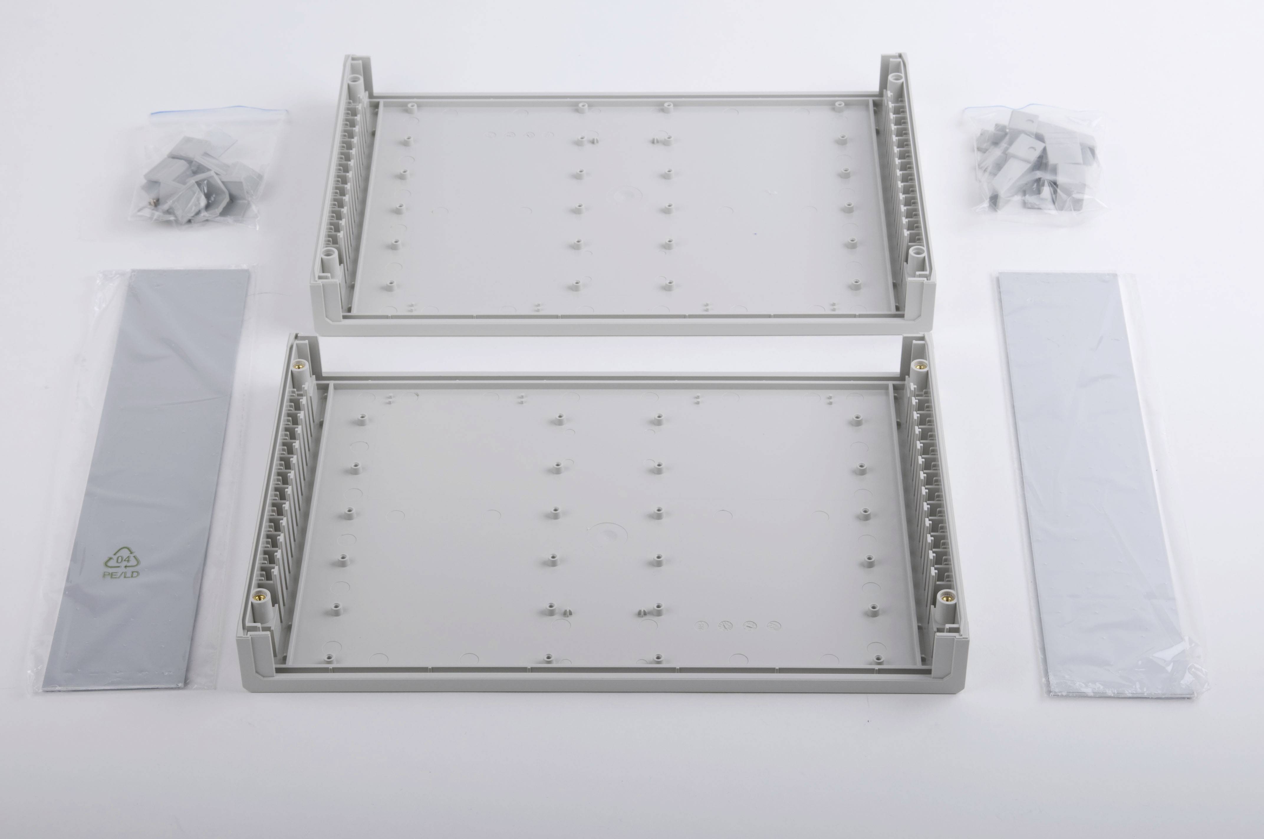 'Deux supports rectangulaires gris en plastique avec des trous de vis, entourés de sets de vis en sachets et de deux bandes de plastique oblongues.'