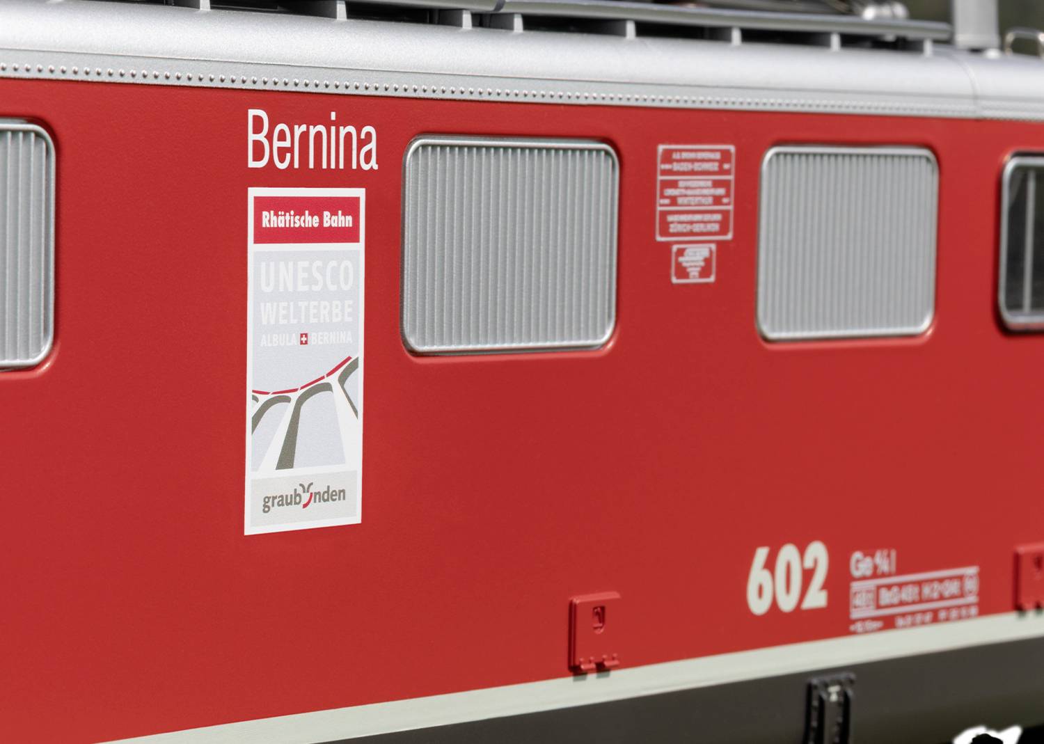 Train rouge portant l'inscription 'Bernina'. Affiche indiquant 'Patrimoine mondial de l'UNESCO'. Modèle du Chemin de fer rhétique, numéro 602, originaire des Grisons.