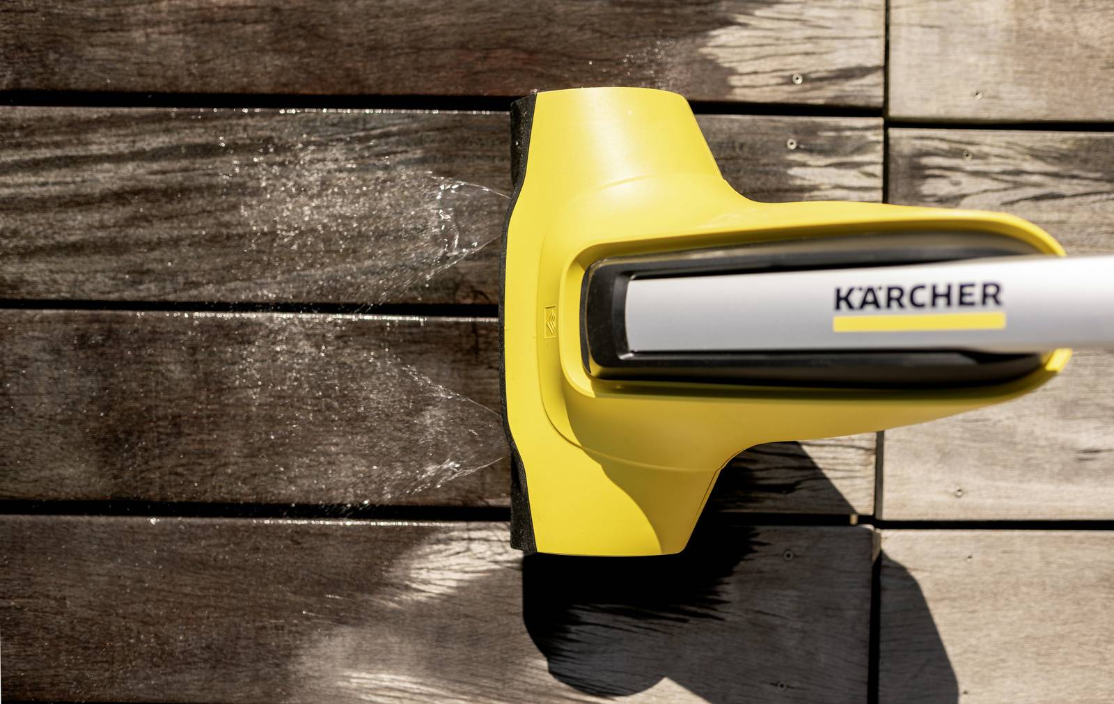 Un nettoyeur haute pression jaune retire les salissures des planches en bois. À gauche, surface nettoyée, à droite non nettoyée et sale.