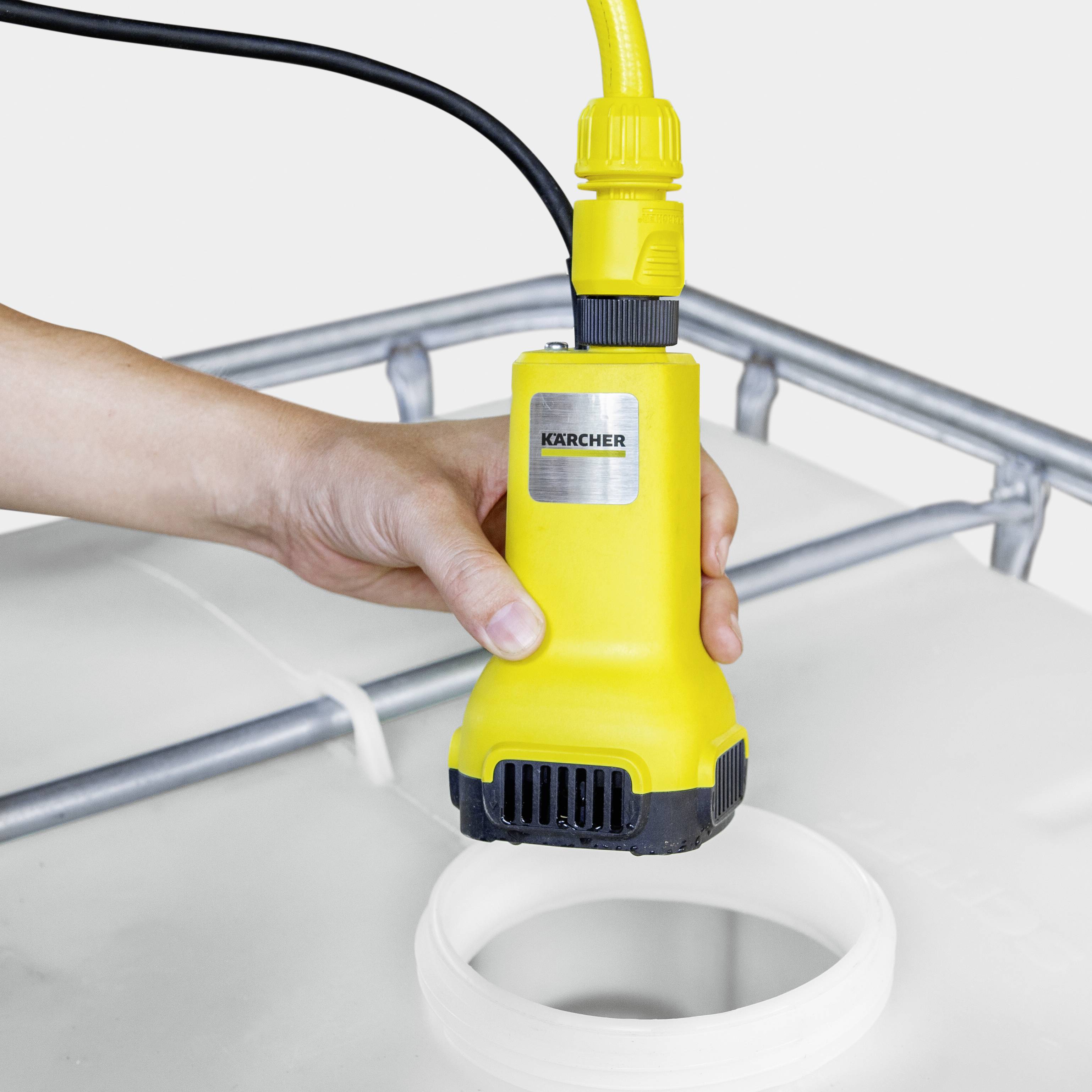 Une main tient une pompe à eau jaune avec un socle noir au-dessus d'un réservoir d'eau. La pompe porte le logo d'un fabricant bien connu.