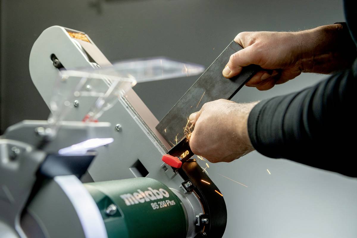 Une personne ponçe une pièce métallique sur une machine à meuler. Des étincelles volent pendant que le bord est poli.