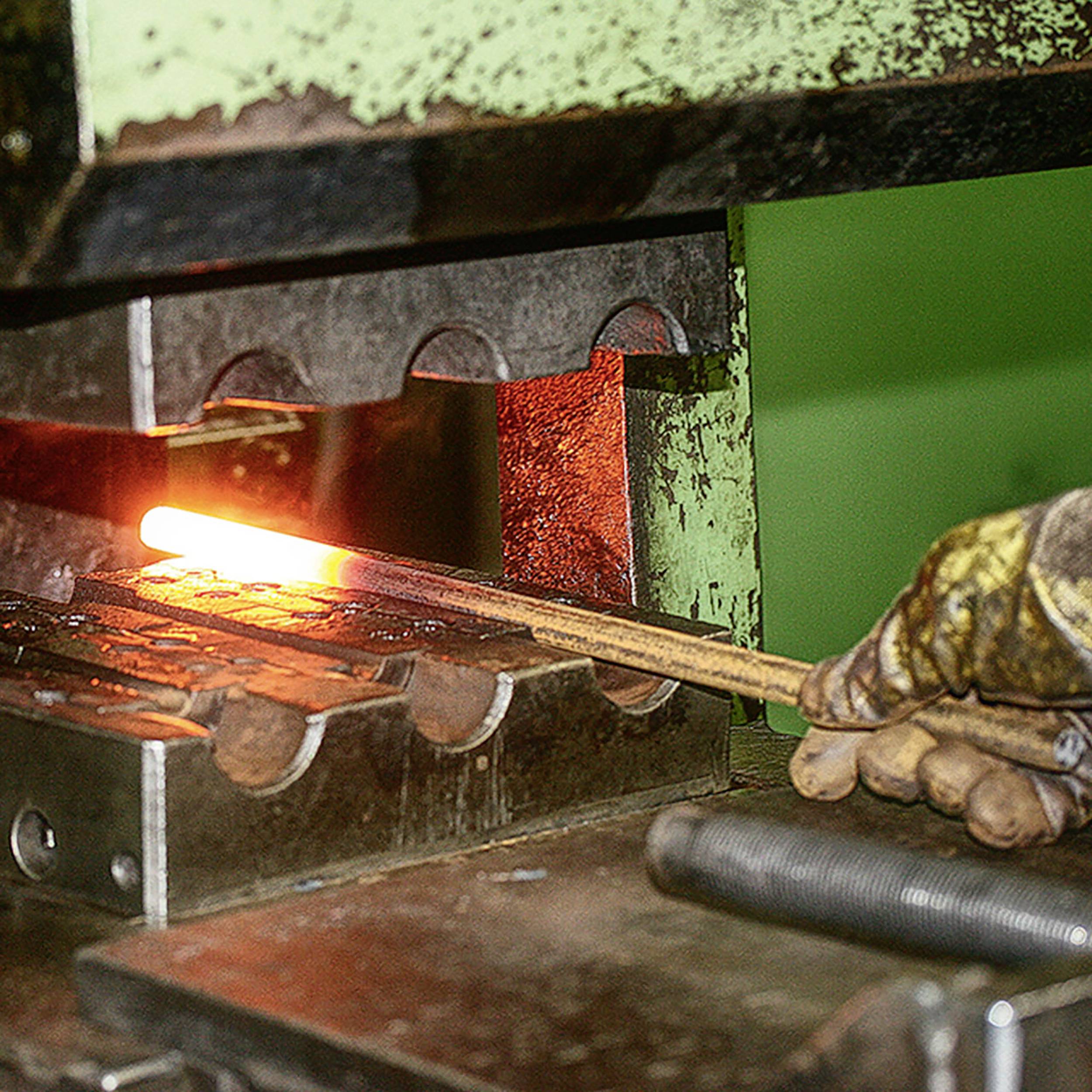 Une presse métallique façonne un morceau de métal incandescent, tenu par une personne portant des protections, dans un environnement d'atelier.