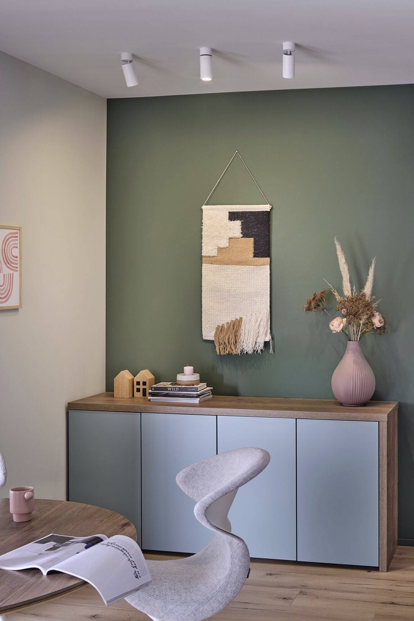 Salon moderne aménagé avec un sol en bois. Un buffet, décoré de livres, de vases et d'une tapisserie murale, est placé devant un mur vert.