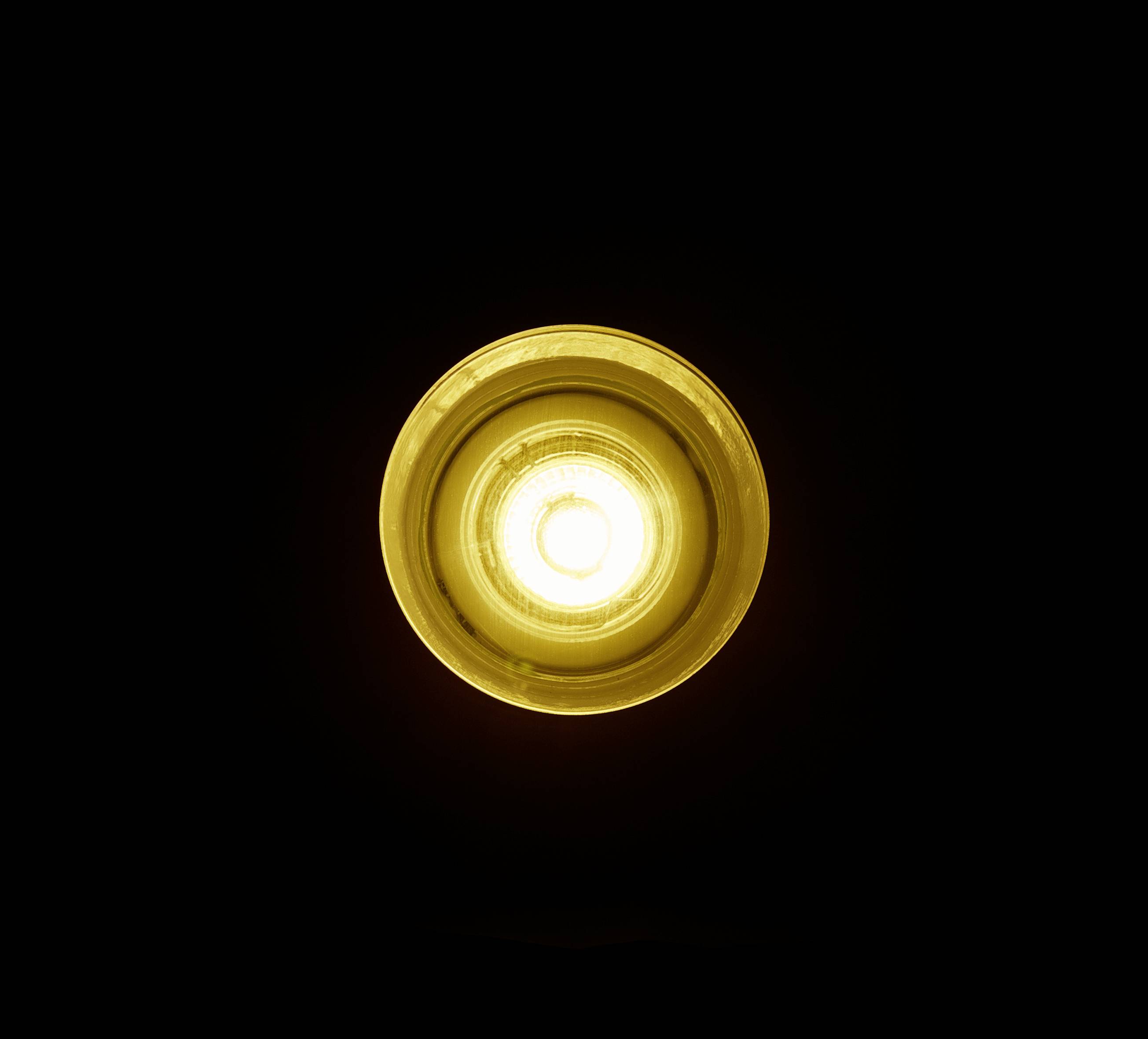 Une unique ampoule allumée diffuse une lumière jaune chaleureuse dans une pièce sombre.