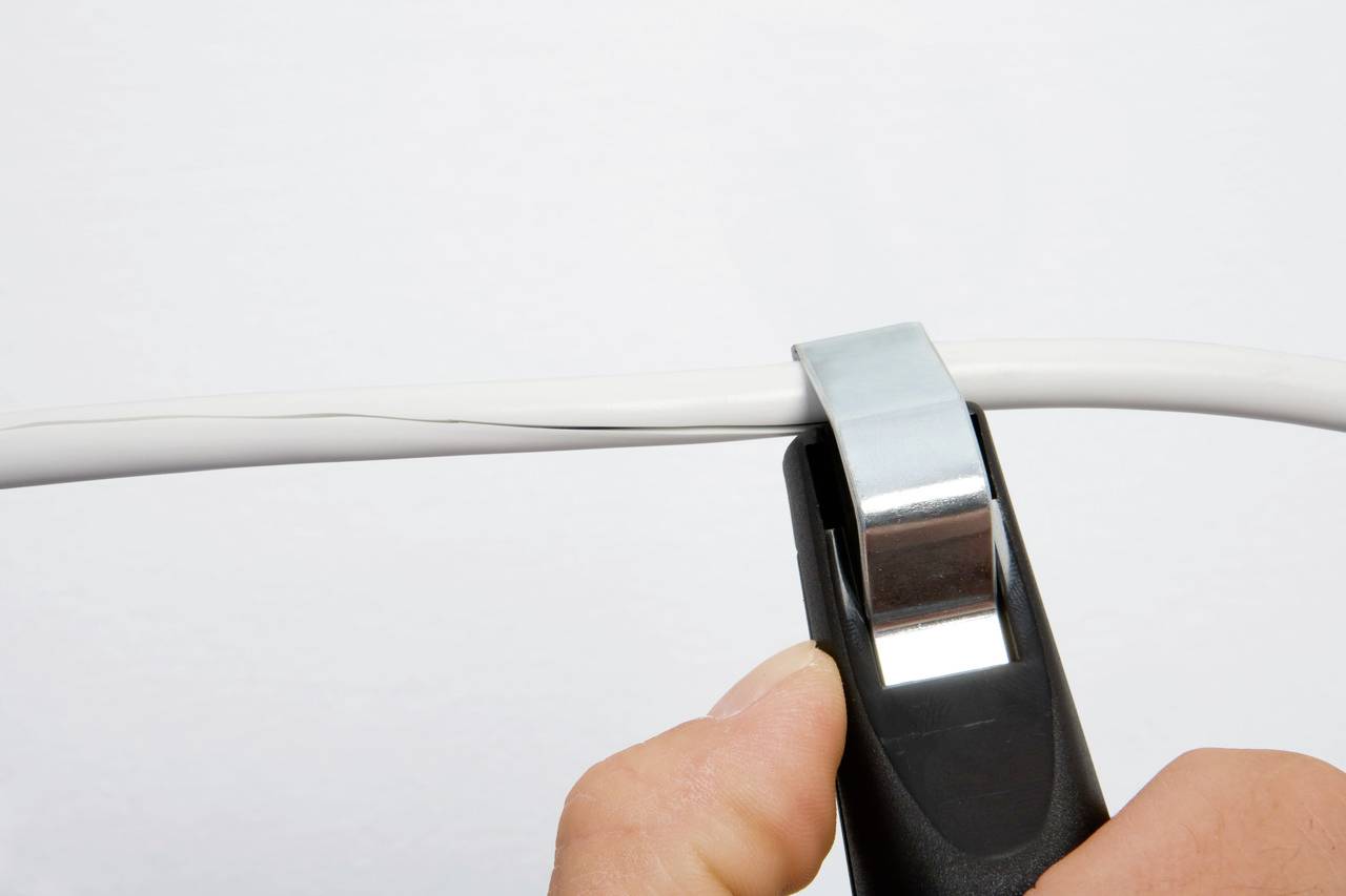 Une main utilise un dénudeur pour enlever l'isolation d'un câble électrique.