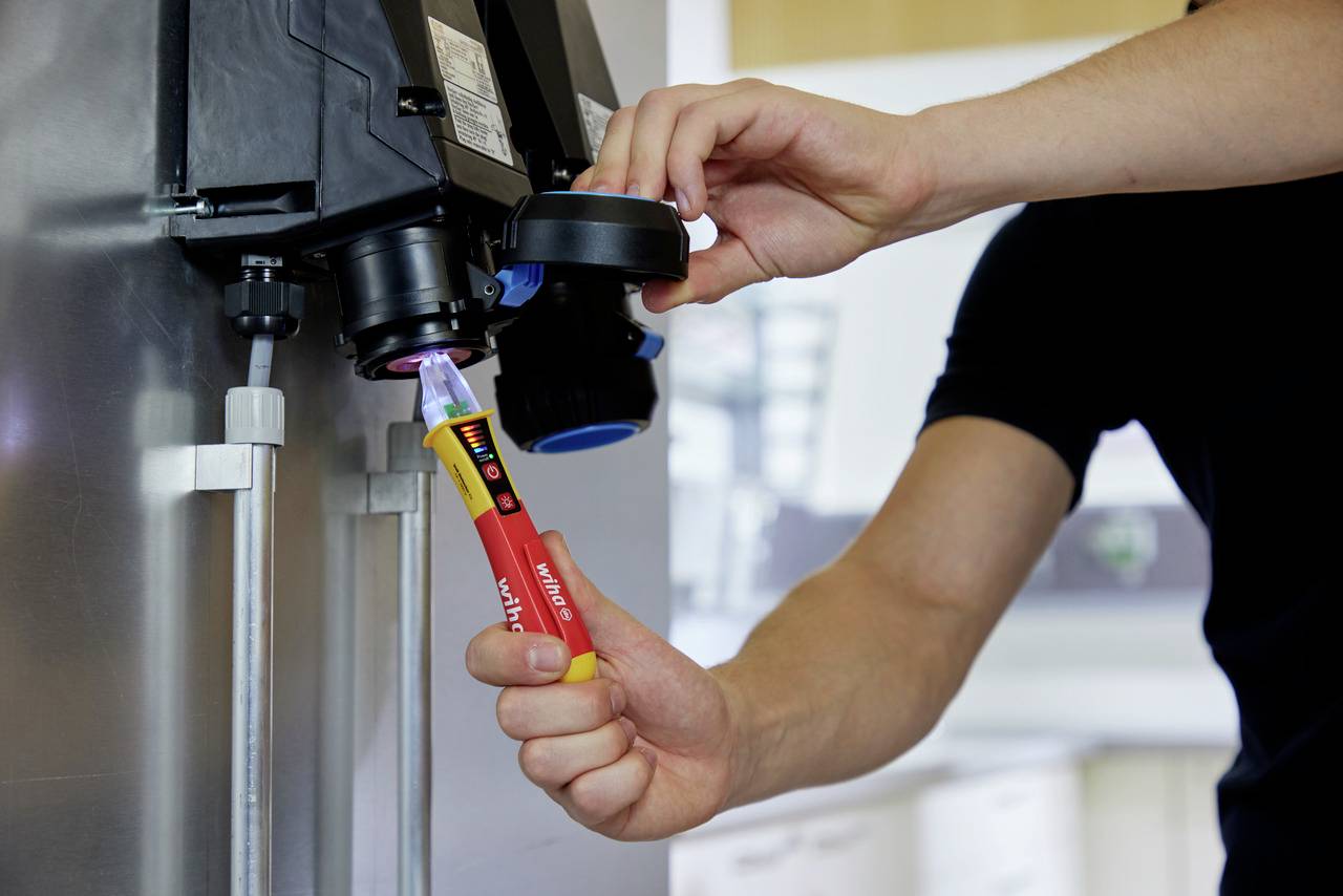 Une personne utilise une machine à gazéifier et tient une bouteille de soda rouge en dessous pour la remplir d'eau.