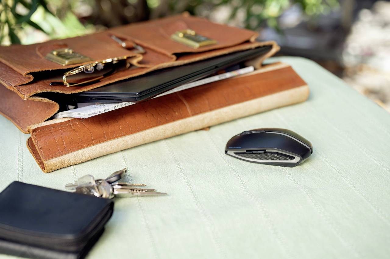 Sacoche marron pour ordinateur portable avec un ordinateur ouvert et des documents, à côté d'une souris noire, un trousseau de clés et un portefeuille sur une table.