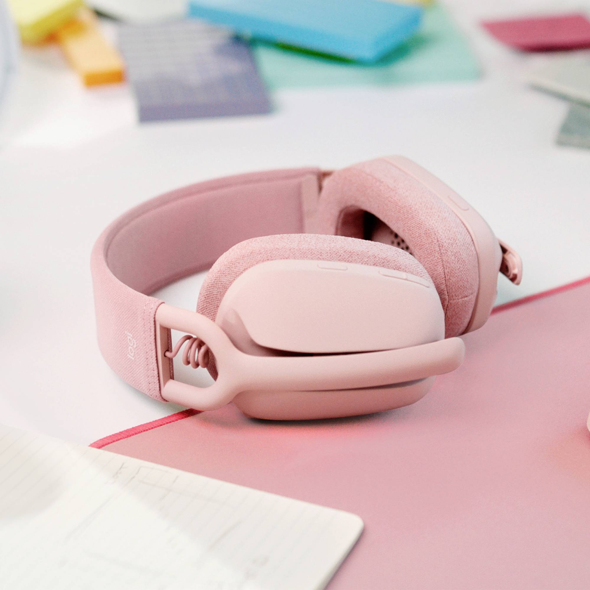 Un casque rose est posé sur un bureau blanc, entouré de papiers et de blocs-notes.