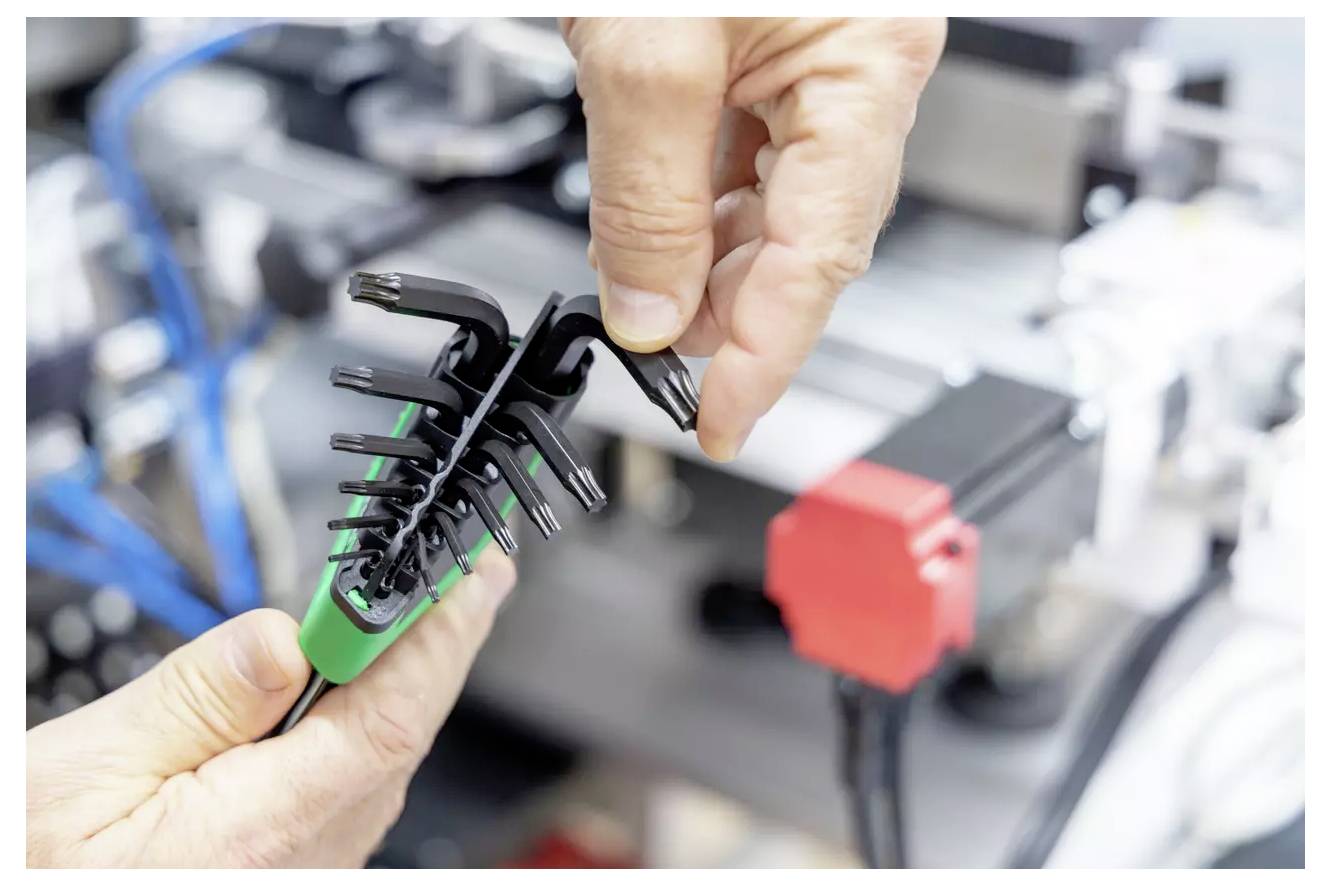 Une personne utilise un collier de serrage noir pour sécuriser des câbles organisés avec un clip vert, sur un fond flou de machines.
