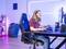 Une personne est assise à un bureau et joue sur un ordinateur, entourée de lumières colorées et d'un équipement de jeu confortable.