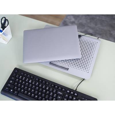 Un ordinateur portable fermé posé sur un refroidisseur sur un bureau avec un clavier. Un porte-stylos est visible en arrière-plan.