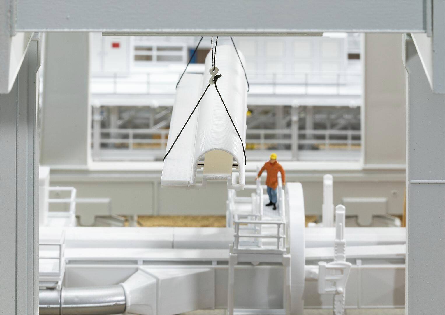 Modèle d'une installation industrielle avec un ouvrier à l'échelle, debout sur une plateforme ; au premier plan, une structure suspendue au-dessus du sol.