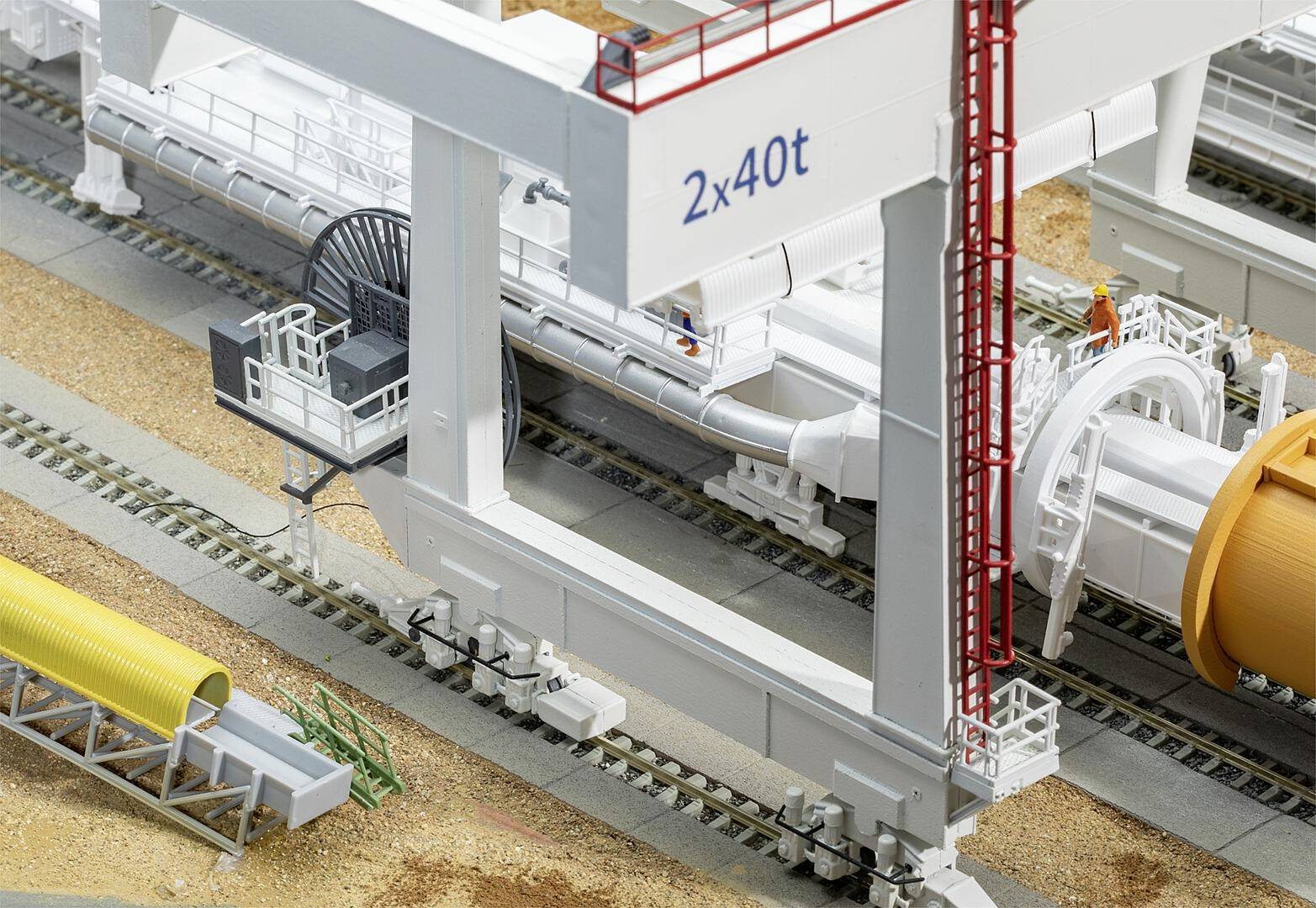 Un modèle représente une installation industrielle avec des rails, une grande structure de grue portant l'inscription '2x40t' et des tubes. Une personne se trouve en haut.