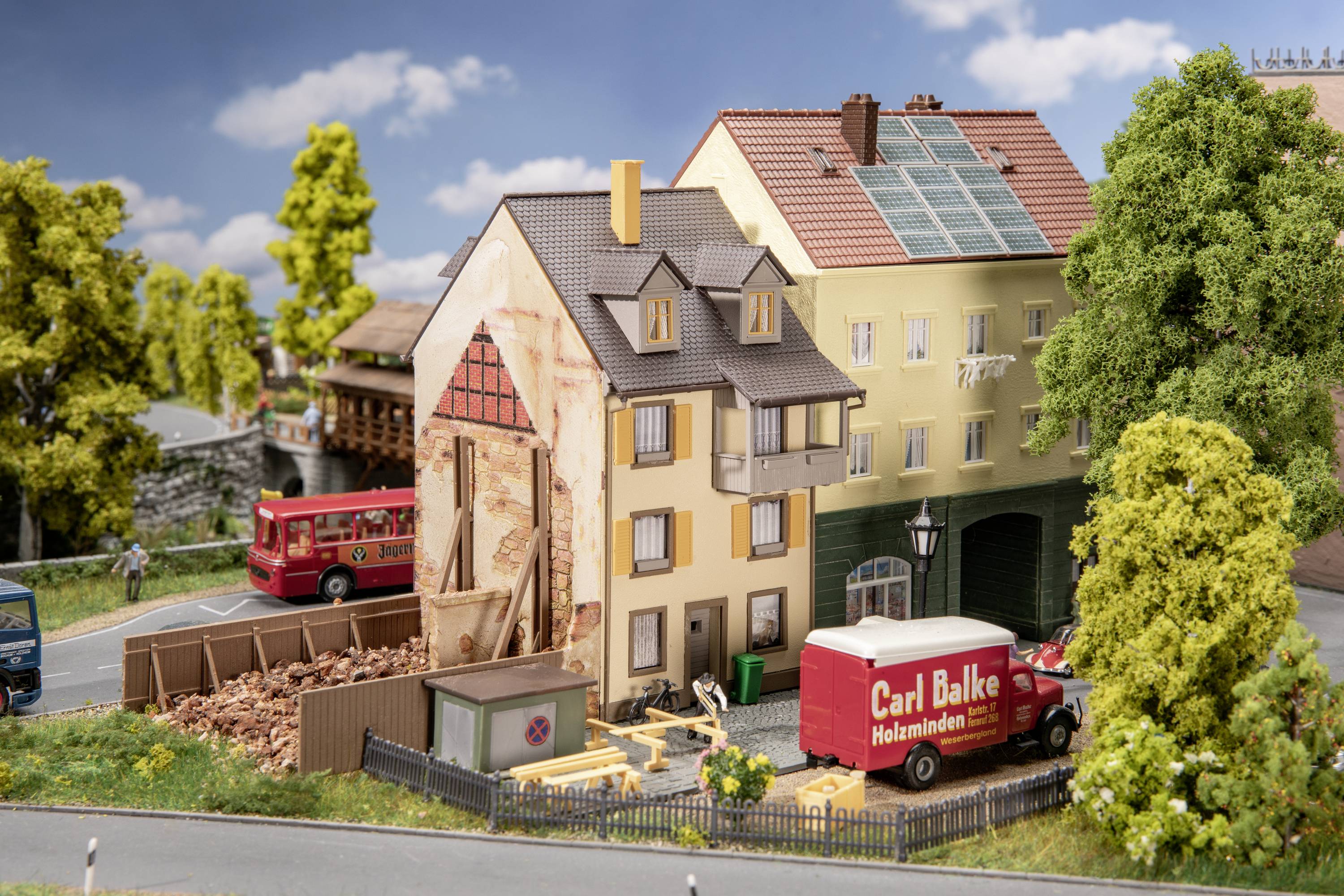 Un village miniature montre une maison en construction avec des matériaux de chantier. Un fourgon rouge portant l'inscription 'Carl Balke'.