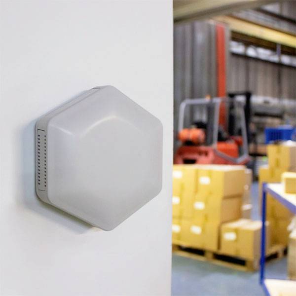 Un capteur hexagonal sur le mur dans un entrepôt avec des cartons et des étagères en arrière-plan.