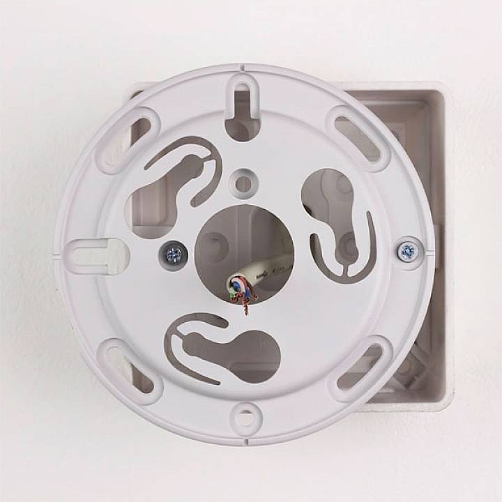 Une plaque de montage ronde blanche fixée au mur pour l'installation d'appareils électroniques ; un câble est visible au centre.